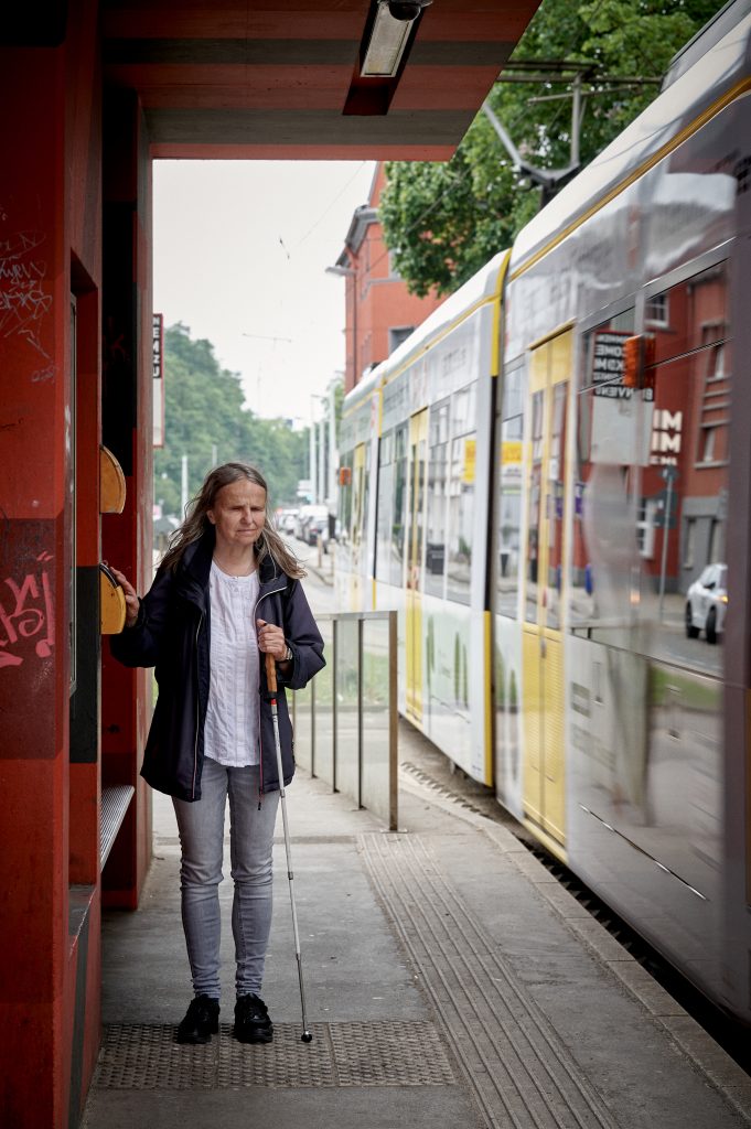 Barrierefreie Straßenbahnhaltestelle. Blinde Frau mit Blindenstock nutzt taktile Bodenmarkierungen.