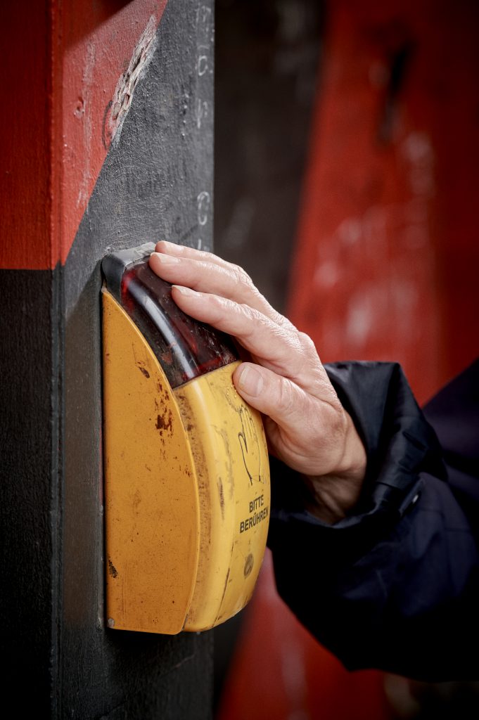 Hand drückt gelben Taster für Sprachausgabe. Symbol für Barrierefreiheit und Orientierungshilfe im öffentlichen Raum.