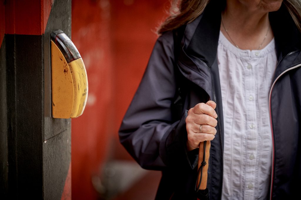 Blinde Frau steht mit Langstock am Taster mit Sprachausgabe.