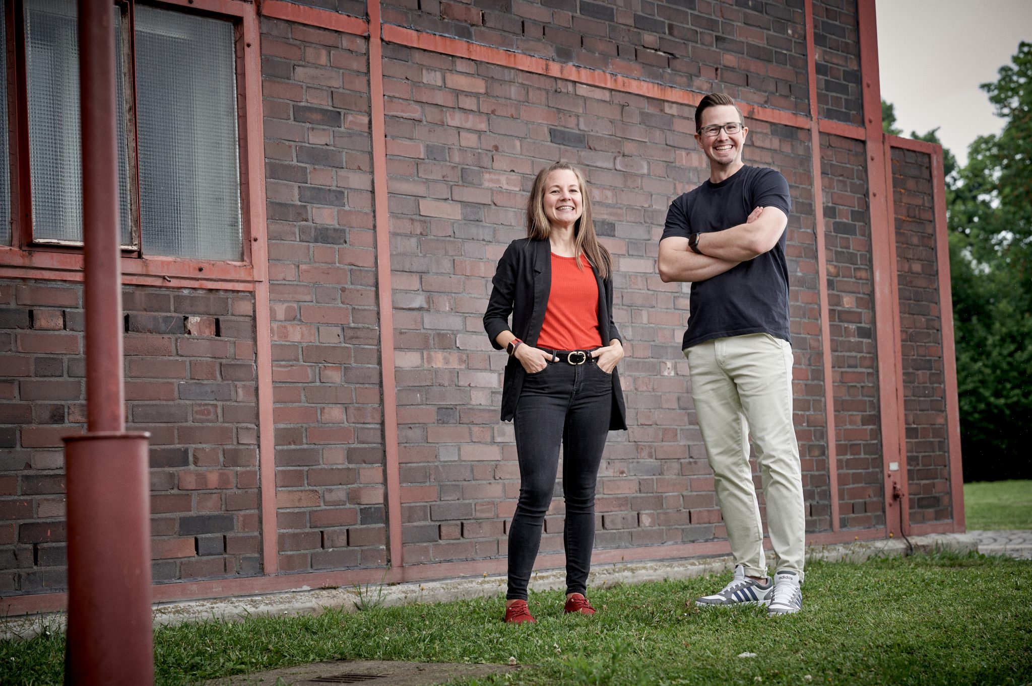 Ein Rehalehrer und eine Rehalehrerin stehen an einer Backsteinmauer und lächeln.